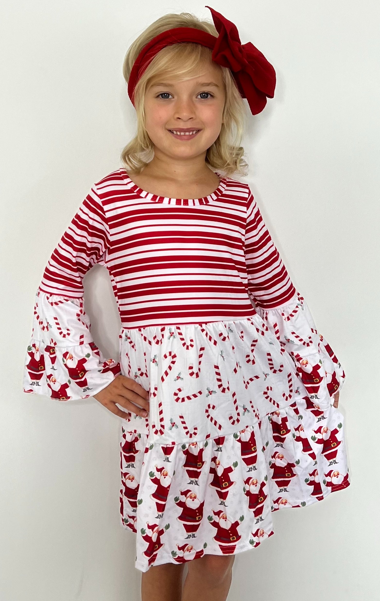 This Candy Cane-Santa Triple Ruffle Dress is a must-have for the holiday season. This adorable dress features a 3 pattern print of stripes, candy canes and Santa, a bell sleeve, and an elegant A-line design. Perfect for any little one this festive season! 🍭🎅