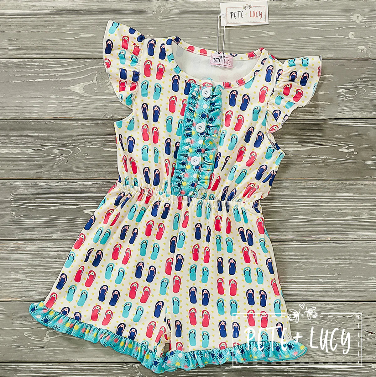 Escape the everyday and hit the beach in style with this whimsical shortie jumpsuit! Featuring a jewel neckline, flutter sleeves, and button and ruffle accents, this one-piece will make you look like a million (sandy) bucks. The garterized waist offers a secure, comfortable fit while the ruffle hem adds a bit of flirty fun. Time to hit the shore!