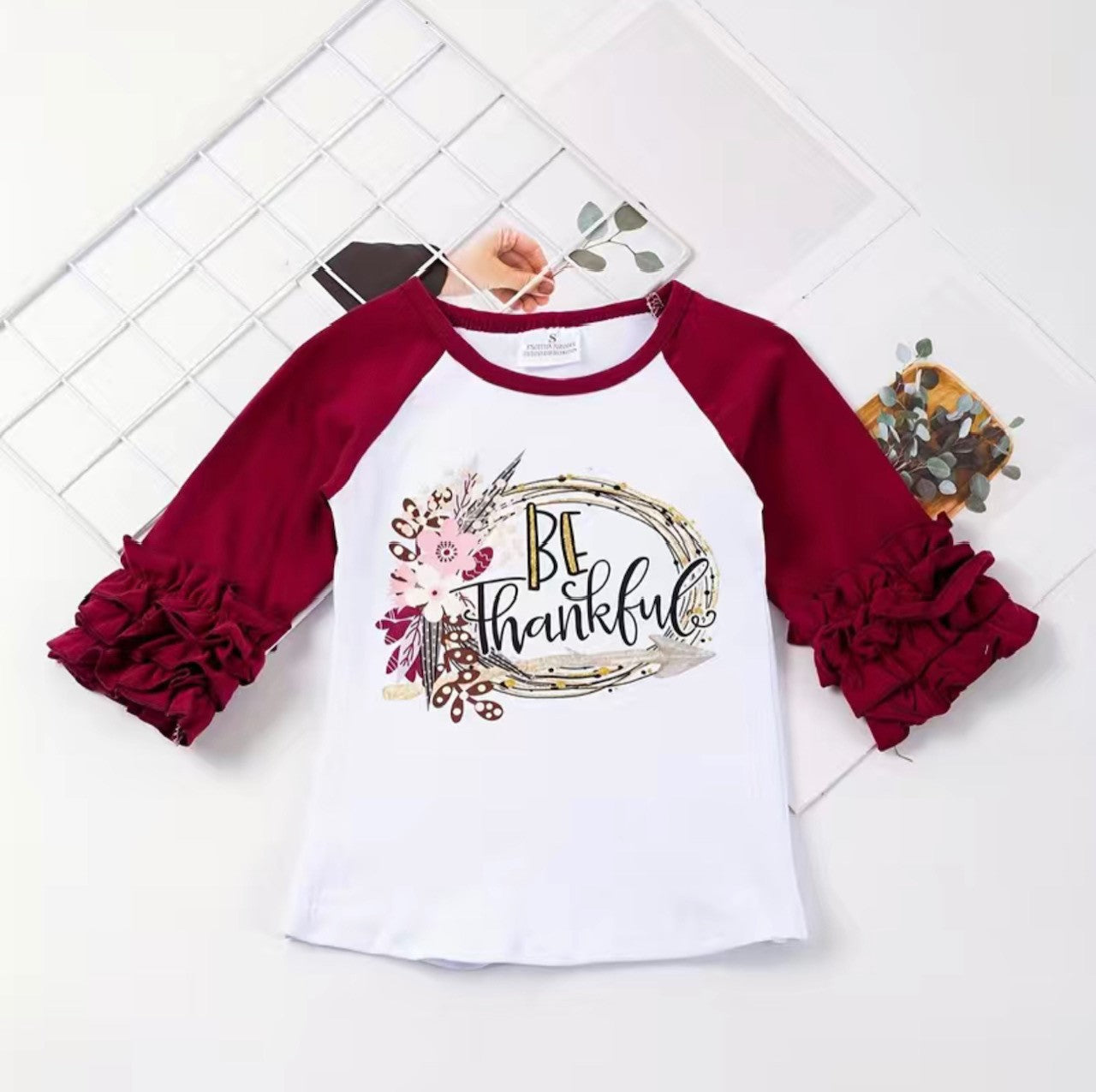 Bring a little extra floral flair and gratitude to your wardrobe with this Be Thankful Raglan! Featuring a beautiful floral design and “Be Thankful” slogan on the chest, you’ll be looking as gracious as ever. The t-shirt has a white background, maroon 3/4 ruffle sleeve and rounded neck and is made from comfortable cotton fabric, ensuring you stay cozy and stylish all day!